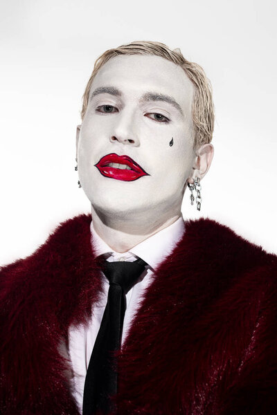 Молодой человек в ярком костюме Джокера с потрясающим макияжем на Хэллоуин.