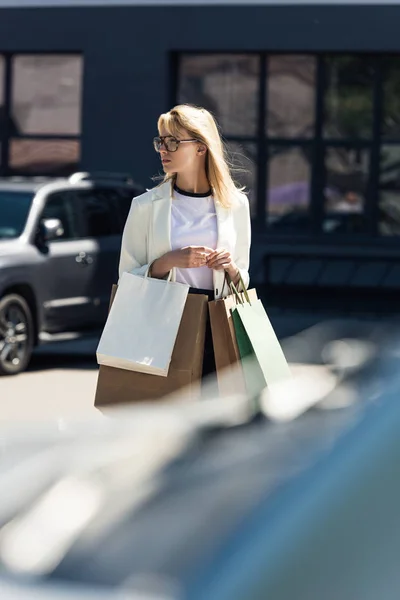 Enfoque selectivo de la joven rubia con bolsas de compras caminando en el estacionamiento - foto de stock