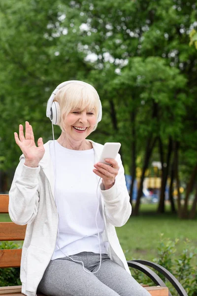 Весела літня жінка слухає музику з навушниками та смартфонами у парку — стокове фото