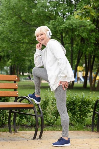 Пожилая спортсменка в наушниках тренируется в парке — стоковое фото
