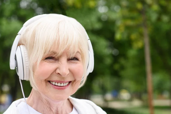 Feliz mujer mayor escuchando música en los auriculares - foto de stock