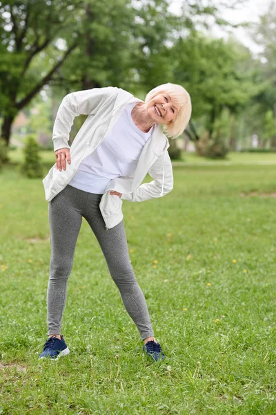 Happy senior sportswoman exercising on green lawn in park — Stock Photo