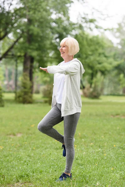 Sonriente deportista de edad avanzada haciendo ejercicio sobre hierba verde en el parque - foto de stock