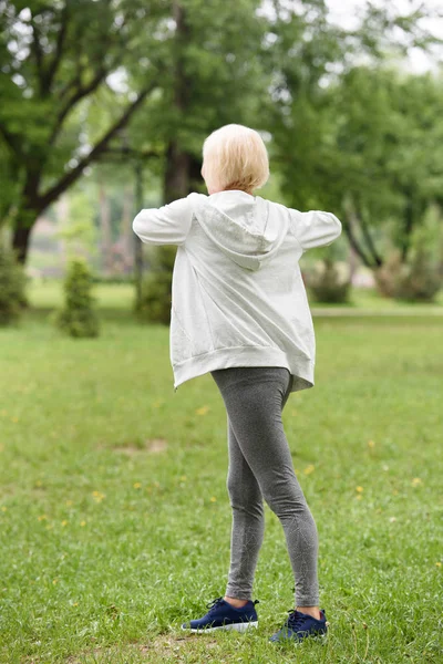 Vista posteriore della donna anziana sportiva che esercita sul prato verde nel parco — Foto stock