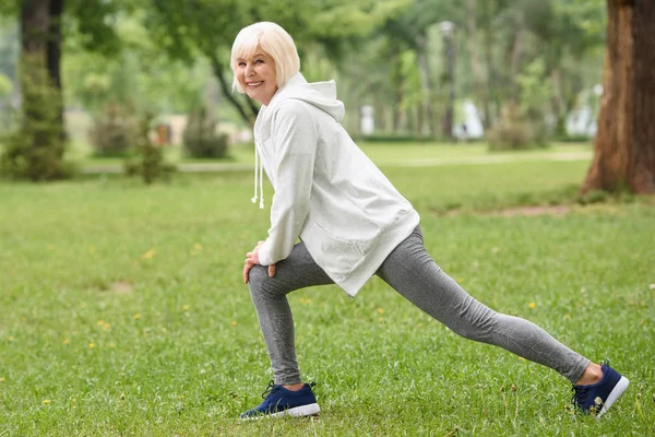 Sorridente anziana sportiva formazione e fare salti sul prato verde nel parco — Foto stock