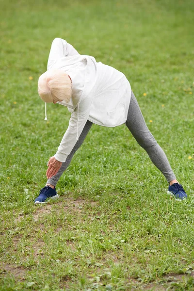 Старша спортсменка, що тягнеться на зеленому газоні в парку, здоровий спосіб життя — стокове фото