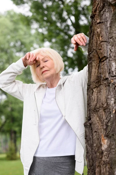 Anziana donna stanca che riposa vicino all'albero nel parco — Foto stock