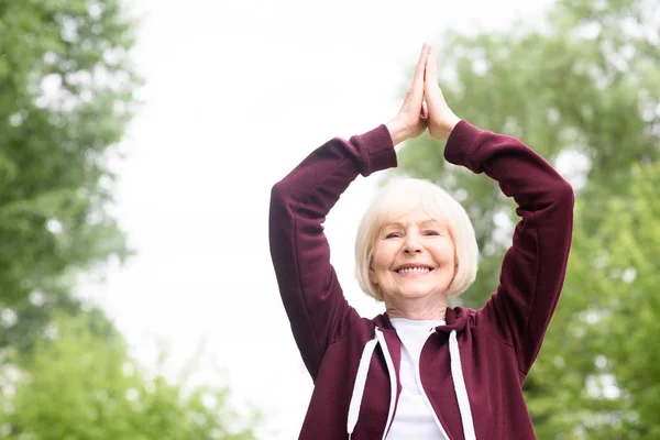 Усміхнена старша жінка практикує йогу в парку — стокове фото