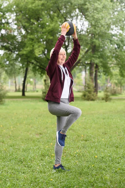 Smiling senior woman training with medicine ball in park — Stock Photo