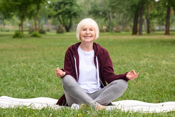 Glückliche Seniorin meditiert mit Gyan Mudra auf Yogamatte im Park — Stockfoto