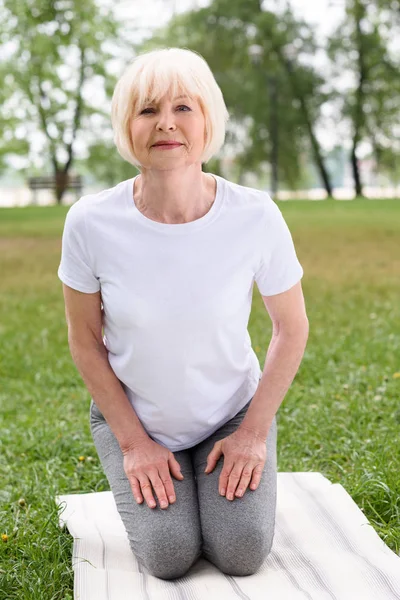 Senior woman practicing yoga on mat on green lawn — Stock Photo