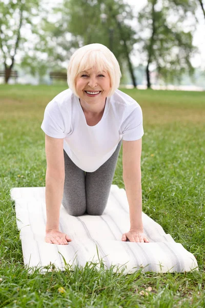 Lächelnde ältere Frau praktiziert Yoga auf Matte auf grünem Rasen — Stockfoto