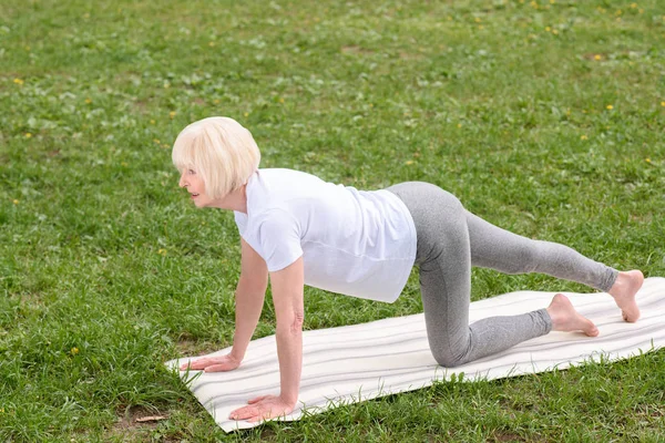 Ältere Frau praktiziert Yoga auf Matte auf Rasen — Stockfoto