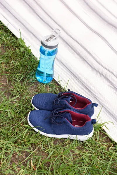Sneakers and sport bottle standing near yoga mat on green grass — Stock Photo