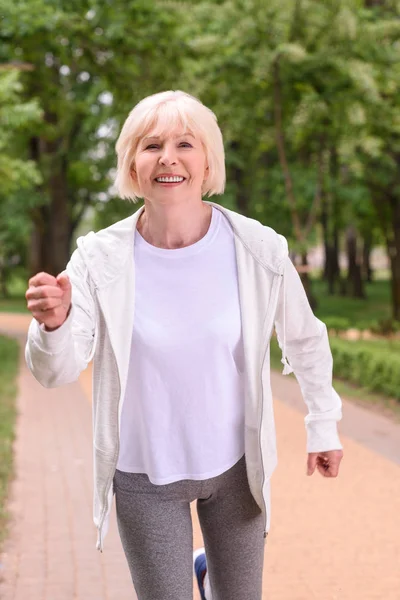 Glückliche sportliche Seniorin joggt im Park — Stockfoto