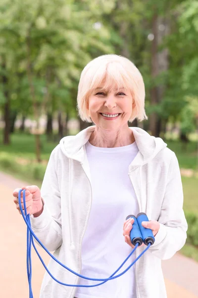 Sportiva anziana sorridente con corda da salto nel parco — Foto stock