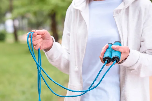 Cropped view of sportswoman holding blue skipping rope in park — Stock Photo