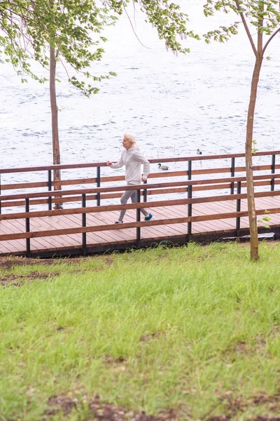 Sênior esportista jogging no caminho de madeira em pak perto do lago — Fotografia de Stock