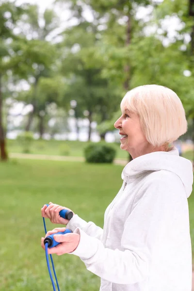 Glückliche Seniorin trainiert mit Springseil im Park — Stockfoto