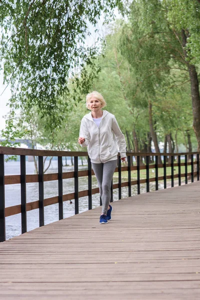 Старшая спортсменка бегает по деревянной дорожке в парке — стоковое фото