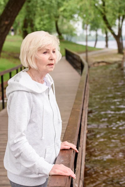 Lonely senior woman standing near railings in park — Stock Photo