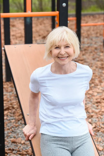 Sportliche Seniorin lächelt und turnt auf Sportplatz — Stockfoto