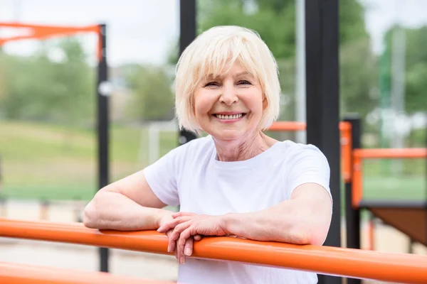 Lächelnde Seniorin steht auf Sportplatz und blickt in Kamera — Stockfoto