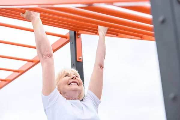 Smiling elderly woman exercising on sports ground — Stock Photo