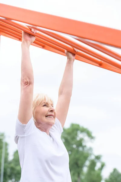 Smiling senior sportswoman exercising on sports ground — Stock Photo