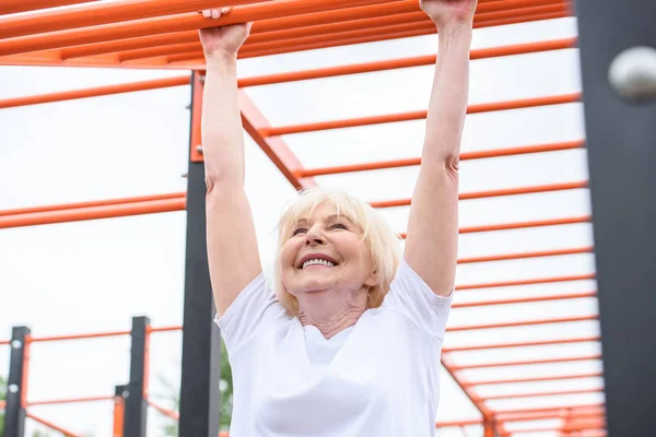 Cheerful senior woman exercising on sports ground — Stock Photo