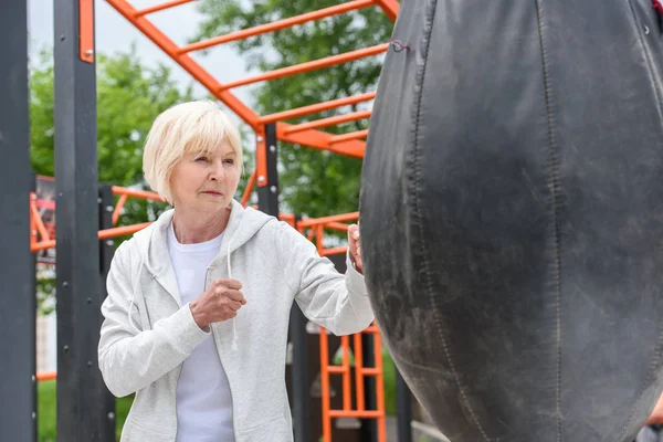 Старша жінка тренується з ударною сумкою на спортивному майданчику — стокове фото