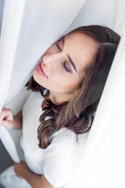 Hochwinkelaufnahme der schönen sinnlichen jungen Frau mit geschlossenen Augen, die hinter einem Vorhang steht — Stockfoto