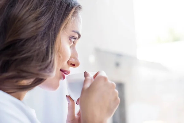 Vista laterale della bella ragazza bruna che beve caffè a casa — Foto stock