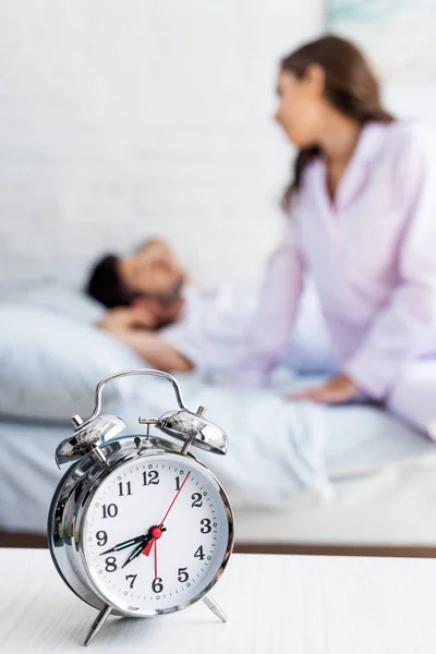 Close-up vista de despertador e casal desfocado em pijama atrás — Fotografia de Stock