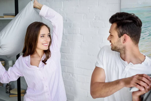 Joven sonriente pareja teniendo almohada lucha en dormitorio - foto de stock