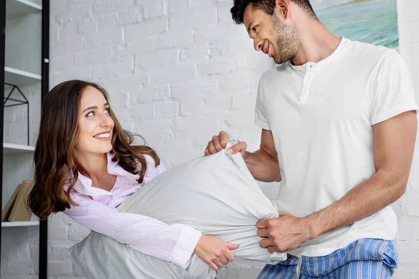 Молодая счастливая девушка и парень веселятся и дерутся с подушками в спальне — стоковое фото