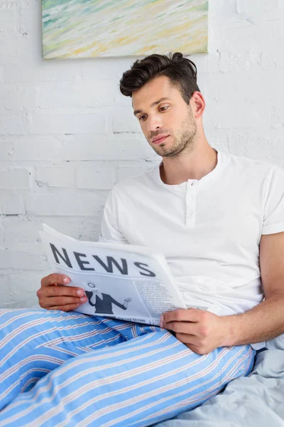 Homem de pijama sentado na cama e lendo jornal de manhã — Fotografia de Stock