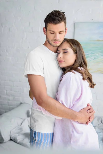 Молодая счастливая пара в пижаме обнимается в спальне — стоковое фото