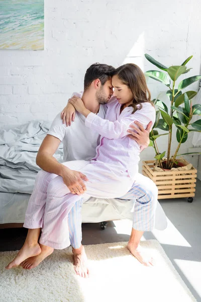 Joven mujer tierna sentada sobre las rodillas de su novio y abrazándolo en la cama - foto de stock