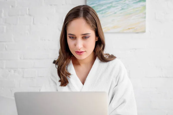 Hermosa mujer en albornoz usando el ordenador portátil en casa - foto de stock