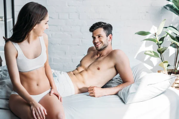 Cariñosa pareja sonriente mirándose en la cama en casa - foto de stock