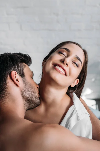 Boyfriend kissing smiling girlfriends neck in bedroom in morning — Stock Photo