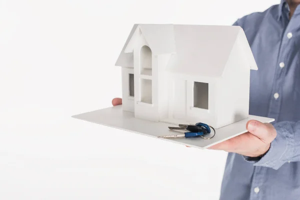 Частковий вигляд людини, що тримає модель будинку і ключі в руках ізольовані на білому — стокове фото