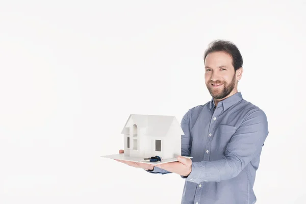 Ritratto dell'uomo barbuto sorridente che tiene il modello della casa e le chiavi nelle mani isolate su bianco — Foto stock