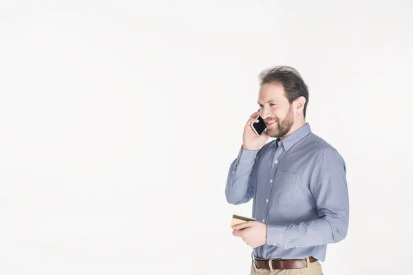 Side view of bearded man with credit card in hand talking on smartphone isolated on white — Stock Photo