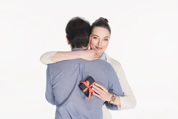 Lächelnde Frau mit eingewickeltem Geschenk in der Hand umarmt Ehemann isoliert auf weiß — Stockfoto