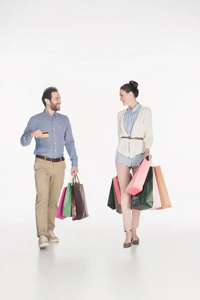 Pareja con bolsas de compras y tarjeta de crédito mirándose aislados en blanco - foto de stock