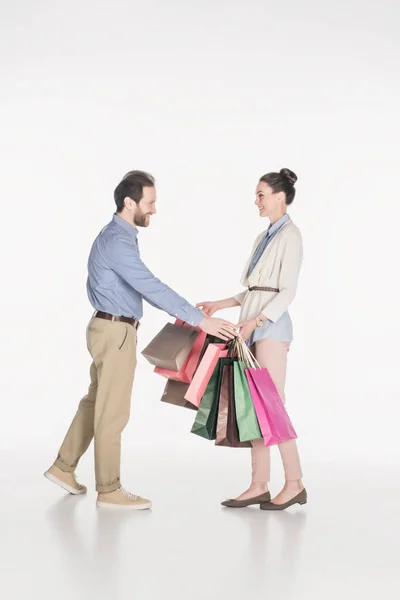 Seitenansicht eines lächelnden Mannes, der Frau Einkaufstüten wegnimmt, isoliert auf Weiß — Stockfoto