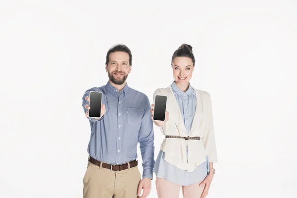 Portrait de couple souriant montrant des smartphones avec des écrans vierges dans les mains isolées sur blanc — Photo de stock