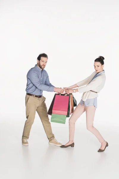 Vue latérale du couple regardant la caméra tout en tirant sur les sacs à provisions isolés sur blanc — Photo de stock